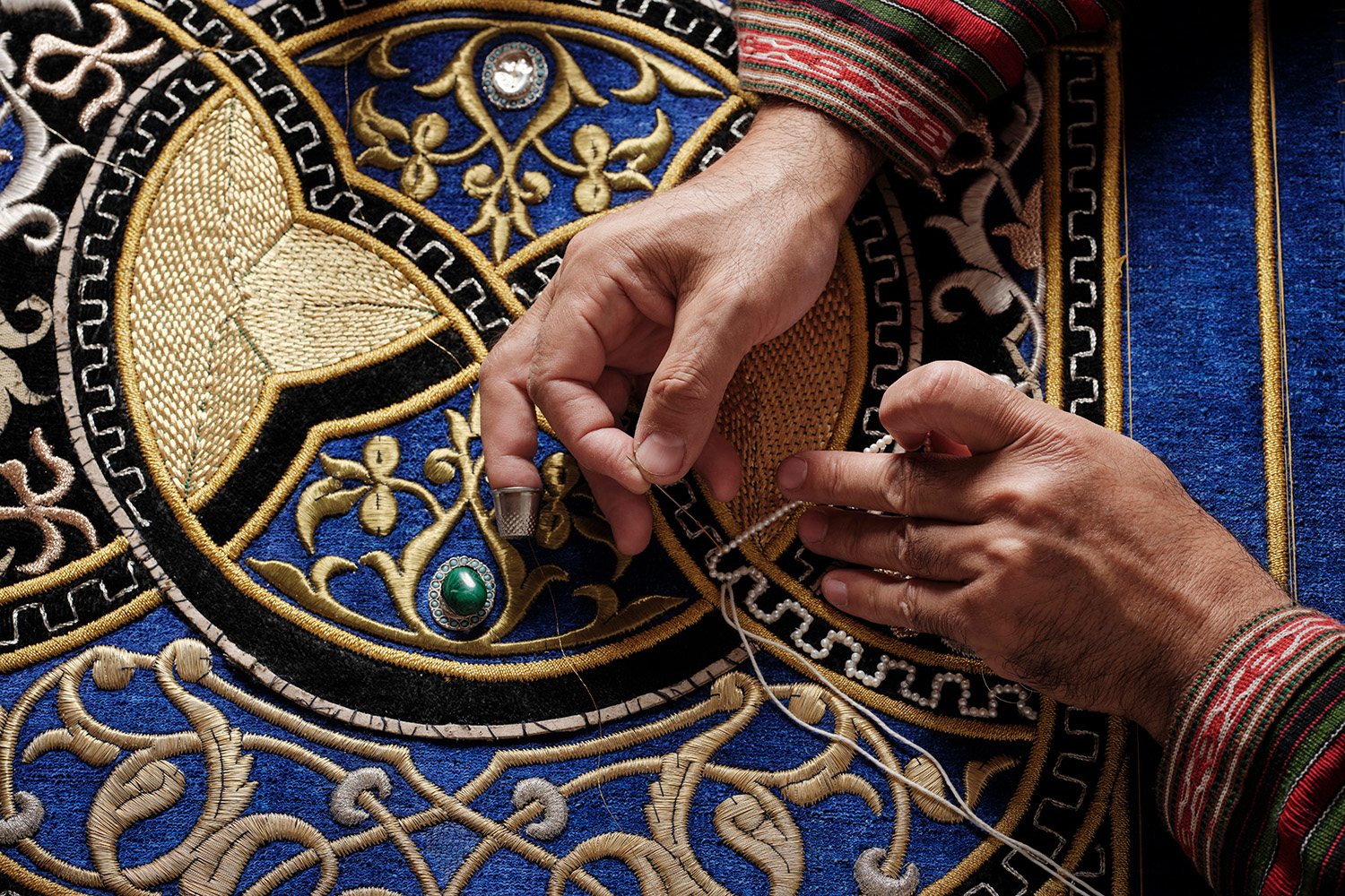 Hands laying gold thread on indigo velvet